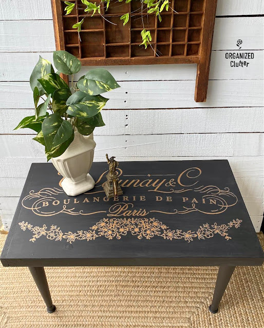 Photo of a thrifted midcentury coffee table painted black with a gold French design transfer.