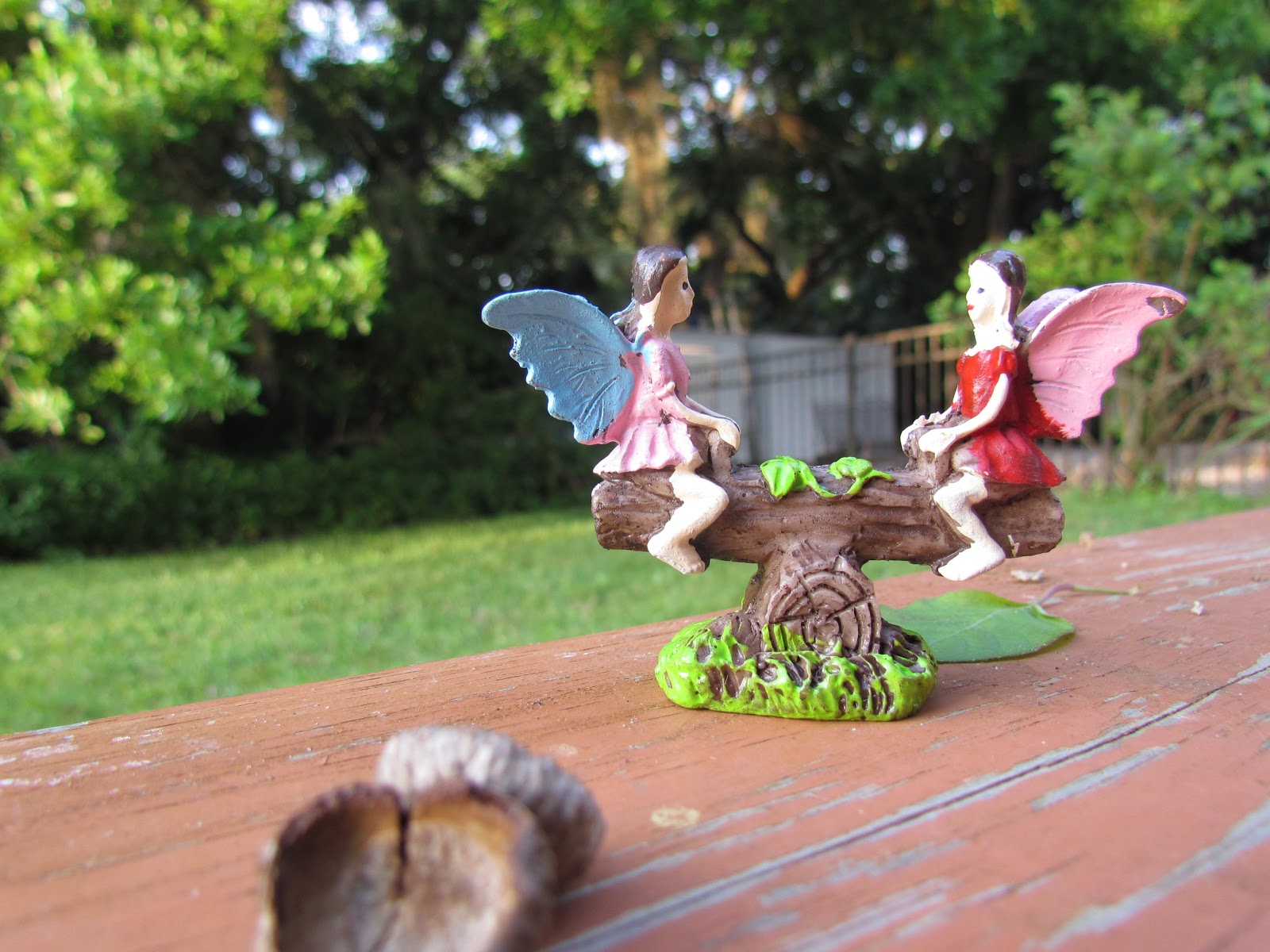 A Tiny Fairy Figurine of Two Fairies Playing Together on a Seesaw Tow in the Tall Grass Amongst the Wildflowers