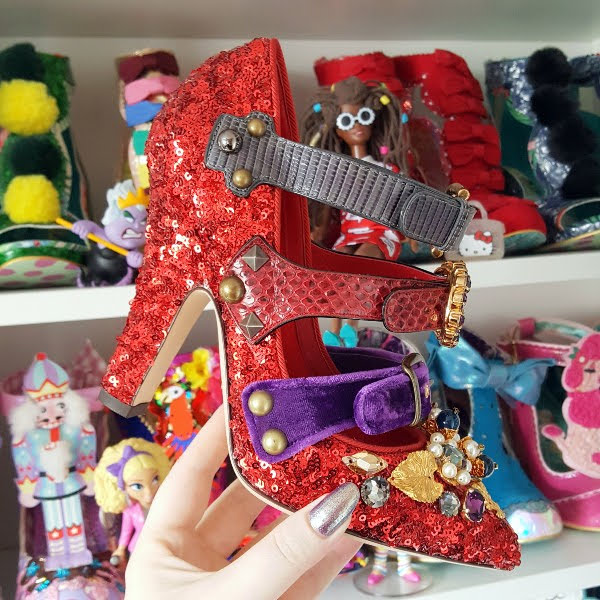 holding red sequins and embellished shoe in hand in front of shoe shelves