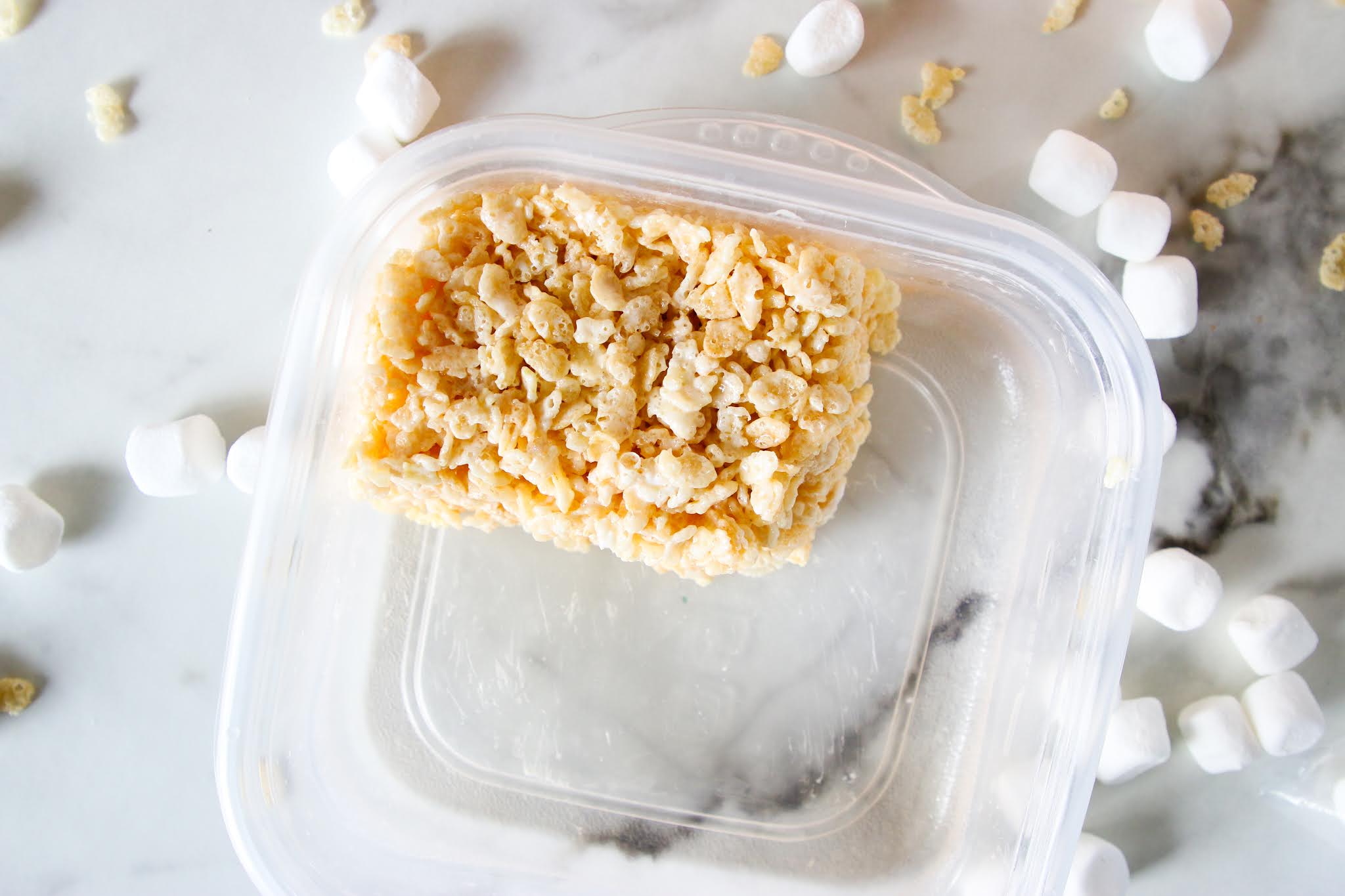 Single serve rice krispie treat Rice krispie treat on a wood platter with a red dish towel with rice krispies and marshmallows scattered on the table
