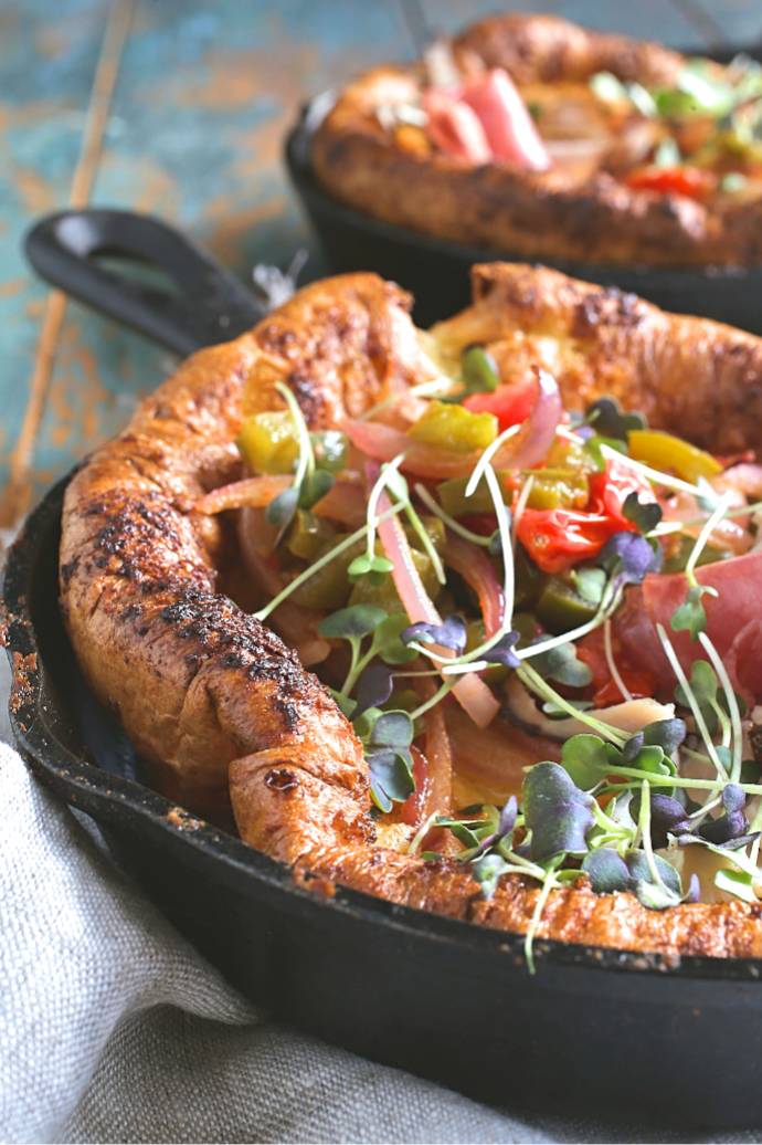 Recipe for a savory Dutch baby German pancake filled with cheese and topped with sauteed bell peppers, red onions, tomatoes and ham.