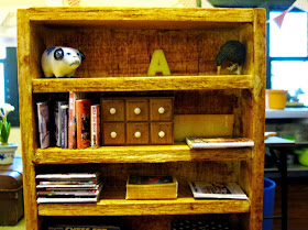 Modern dolls' house miniature bookshelf with books, magazines and a set of spice drawers on display.