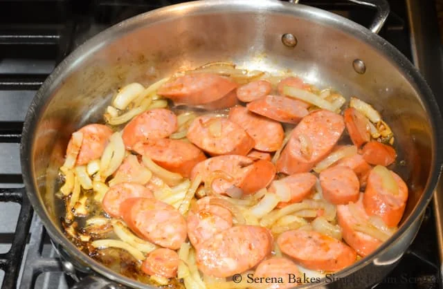 A stainless steel skillet with caramelized onions and sliced andouille sausage.