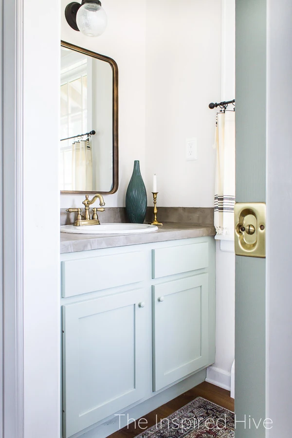 Ocean colored vanity, concrete countertop, brass faucet, and brass mirror in small powder room bathroom