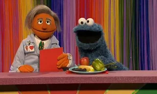 Dr. Ruster and Cookie Monster present the shows Eat Your Colors. Cookie Monster has fruits and vegetables on the plate in front of him. Sesame Street C is for Cooking