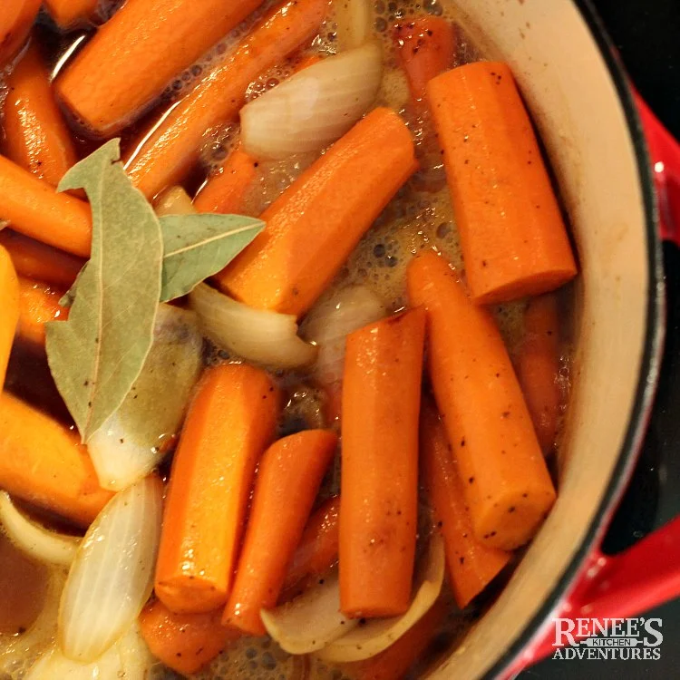 Process photo for Dutch Oven Pot Roast by Renee's Kitchen Adventures carrots and onions with braising liquid and two bay leaves over head view