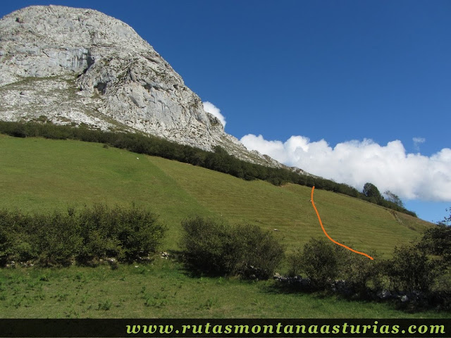 Camino atraviesa pradera hacia la base de la pica