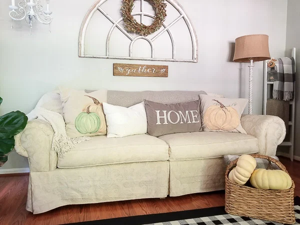 living room sofa with painted pumpkin pillows, basket of pumpkins and antique arch window