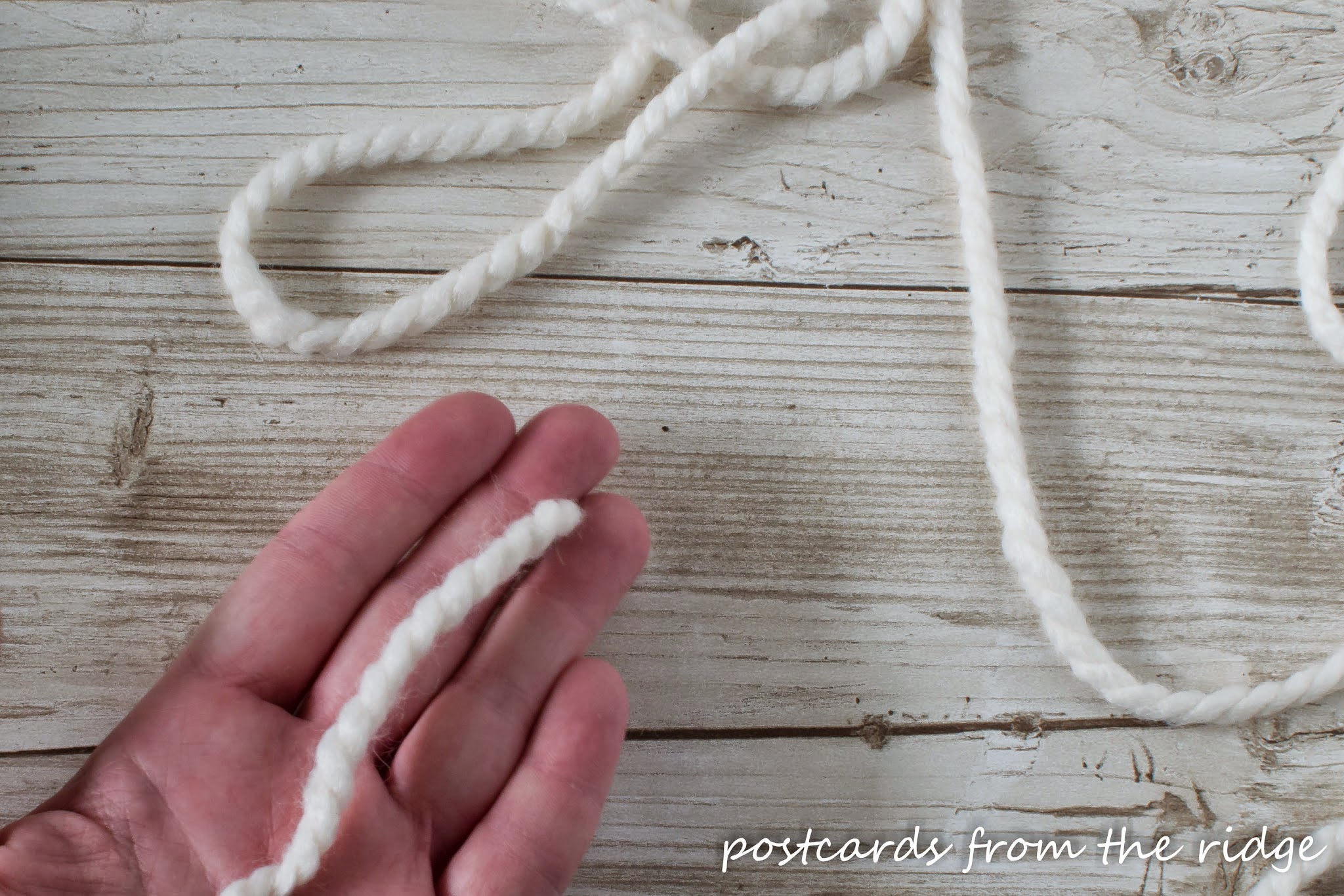 ivory yarn wrapped around hand for pom pom