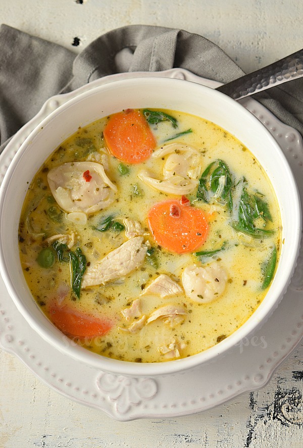 a white bowl on a white background with  chicken tortellini soup with spinach