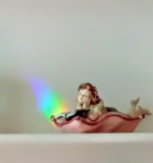 a china figurine looks up from a book, there's a rainbow shining on the wall next to it