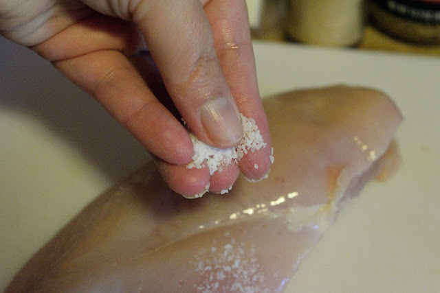 The boneless skinless chicken breast being seasoned.