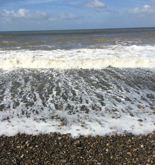 a-picture-of-the-seashore-with-foamy-waves-on-pebbles