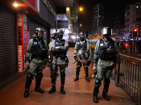 four Hong Kong police officers wearing riot gear — three holding pepper spray canisters