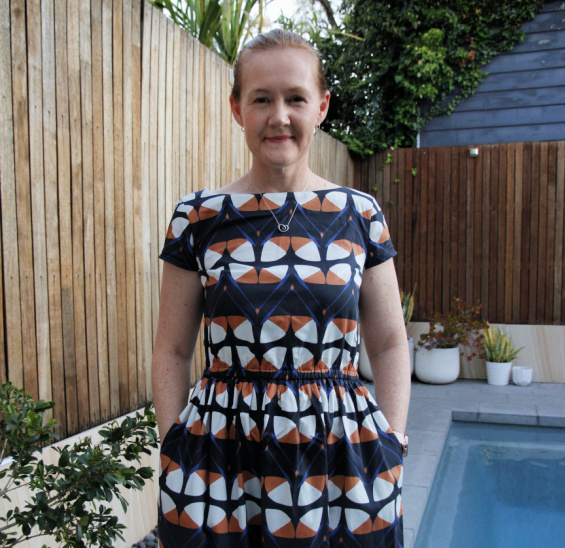 a white lady posing beside a pool in a graphic blue and orange print dress
