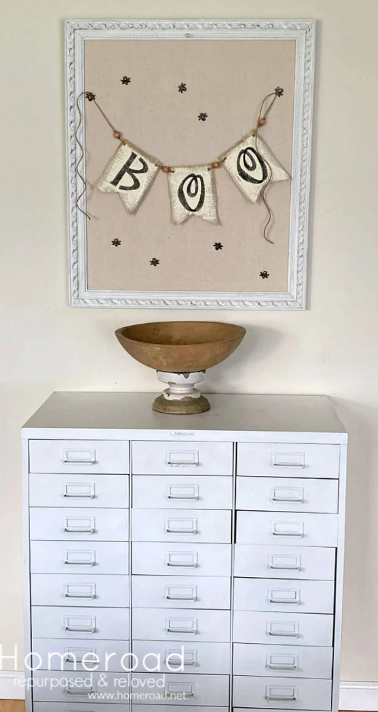 White metal file cabinet with wooden bowl, framed bulletin board and boo banner