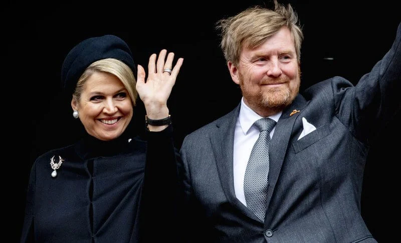 Queen Maxima wore a black wool high collar cape coat. Black leather handbag. Pearl drop earrings and diamond brooch. Gripoix earrings