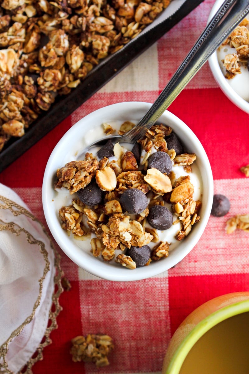 Chocolate Chip Peanut Butter Granola | The Two Bite Club Top view of a white bowl of yogurt topped with Chocolate Chip Peanut Butter Granola on a red and white checkered background.