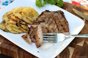 sliced and grilled pork chops on a white platter with grilled pineapple slices on the side