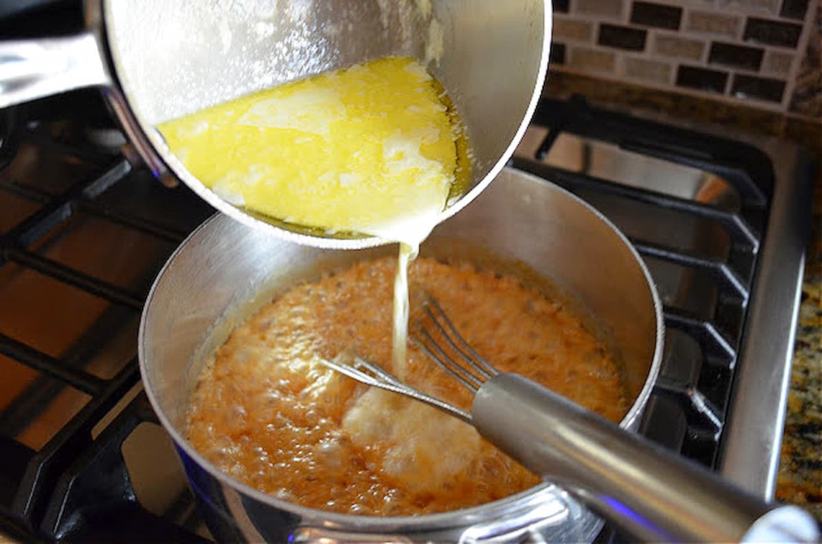 Hot cream and butter mixture being poured into caramel sauce.