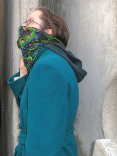 A woman wearing a crochet lace cowl done in a variegated yarn. The cowl is pulled up over her mouth and nose.