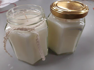 Photograph of two home made candles in jars, one with a gold lid on, the other open and with a ribbon tied around the neck of the jar.