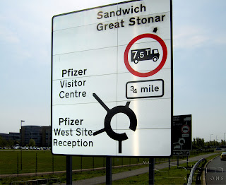 Photograph of a road sign with a white reflective background with black writing and symbols.