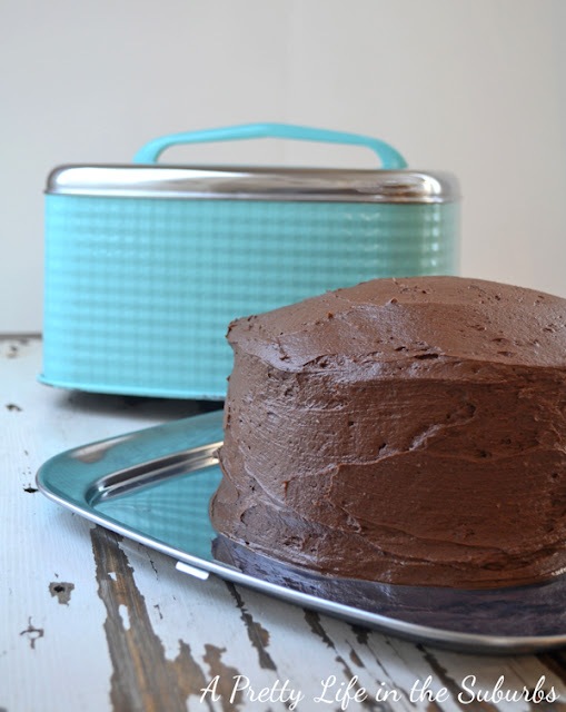 a Chocolate Cake with Chocolate Buttercream Icing sits next to a teal coloured cake pan