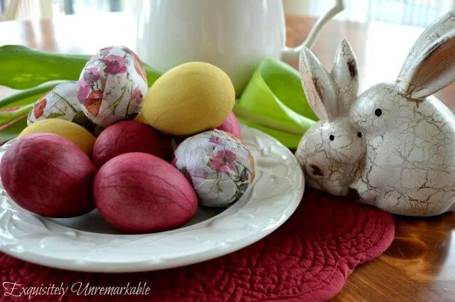 Decoupaged and painted Easter eggs on white plate next to flowers and faux bunnies