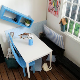View of a one-twelfth scale modern miniature cafe scene, in blue and white with a bird theme. A display shelf has fallen off the wall, with the contents having knocked over several other components of the scene, and edned up on the floor.