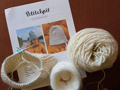 A printed out hat pattern from design PetiteKnit lays on the floor with the the cashmere merino and mohair yarns held together for the beginning of the Stockholm Hat project, knit on a circular needle