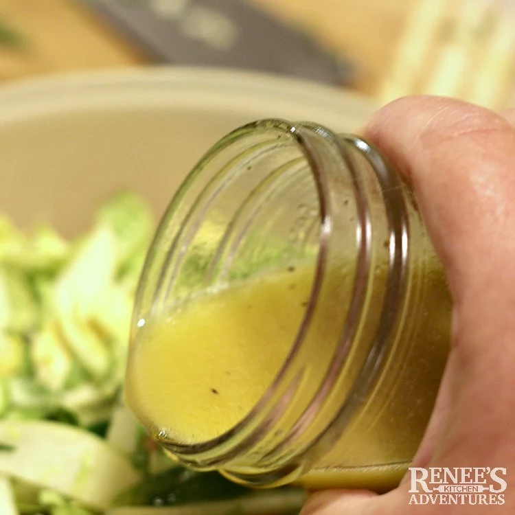 Pouring dressing onto the Shaved Brussels Sprouts Salad with Apples and Ginger