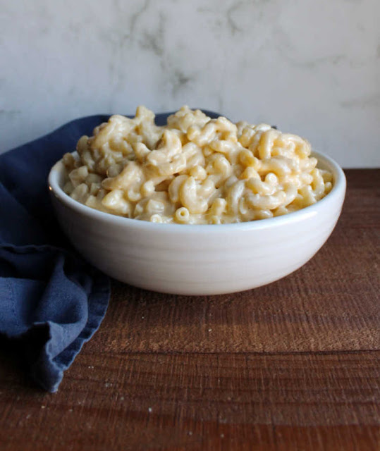 This is the creamiest stovetop macaroni and cheese recipe ever! It is good on it's own or stir in some ham for a simple family pleasing dinner. white serving bowl filled with creamy cheesy mac and cheese