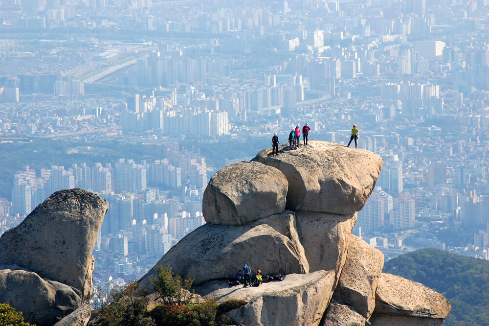 Hikers on a rock to the top with the Seoul city view background in the distance Insubong Peak, Mt. Bukhansan National Park. Best 10 Seoul Attractions | Explore Amazing Things to Do in Seoul