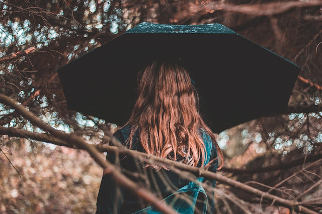 Photo from behind of a person with long hair holding an umbrella under a tree