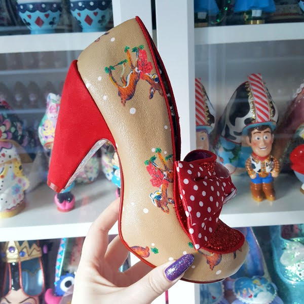 Irregular Choice One Love beige deer print shoe with red suede heel held in hand in front of shoe room shelves