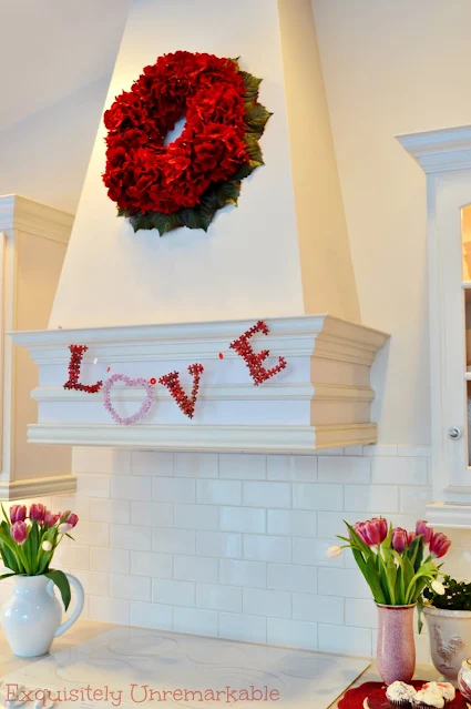 Love Banner For Valentines Day hanging on a kitchen hood with tulips on the counter in vases and a red hydrangea wreath hanging above