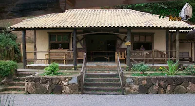 Base com pedra na construção da cabana rústica com os pilares de madeira, a escada de dormente e o muro de pedra rústico.