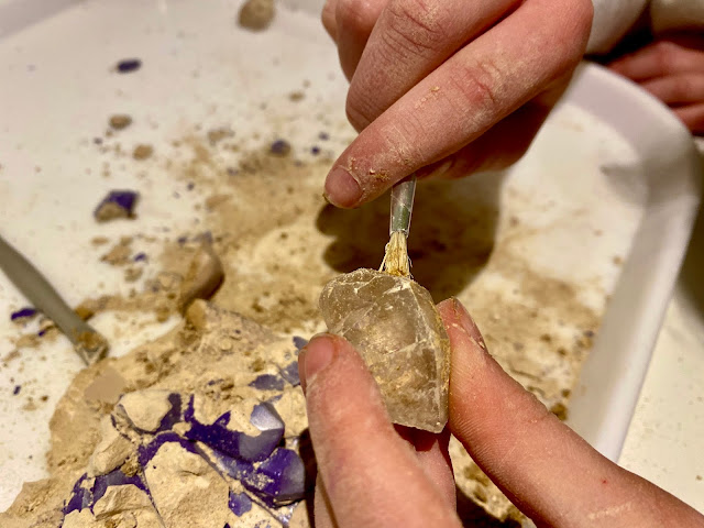 A close up of the dirt being removed from a crystal with a little paint brush