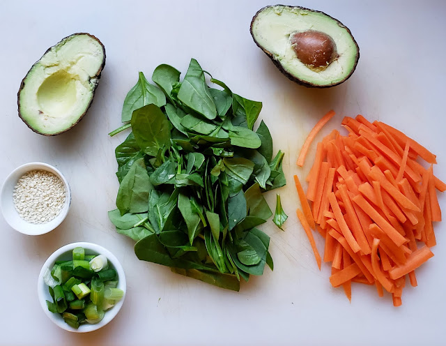 Fresh veggies on a cutting board: avocado, spinach, carrots, sesame seeds, and green onions