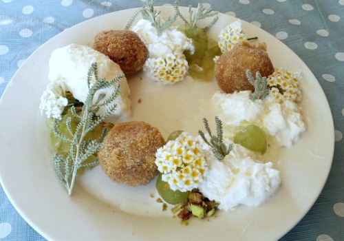 Un plato adornado con flores, croqueta, nata (crema de leche) y helado