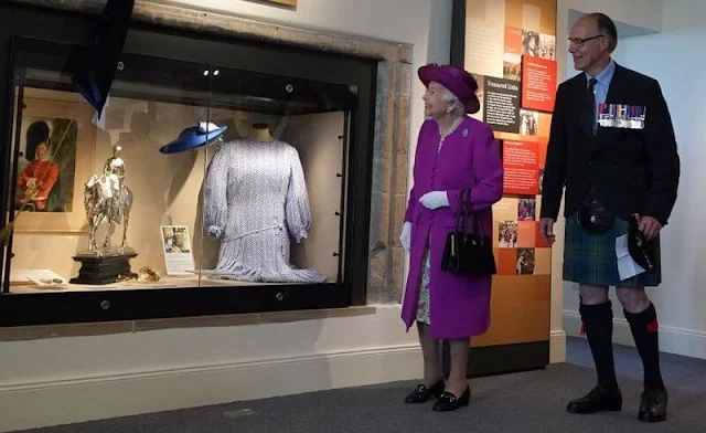 The Queen wore a floral print dress and purple coat and purple hat. diamond brooch