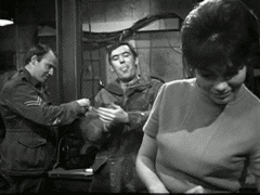 A black and white clip from the Doctor Who TV series. A man in the background is asking a woman in the front," What's a girl like you doing in a job like this?"