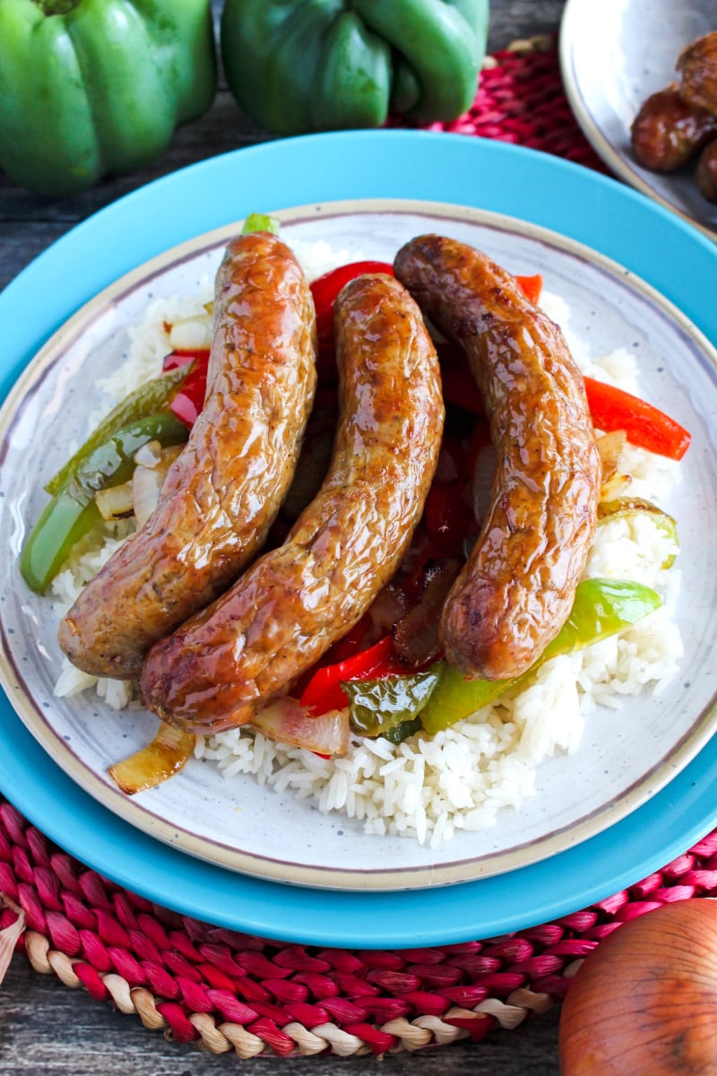 Top view of Air Fryer Sausages over rice, peppers, and onions on a tan and blue plate.