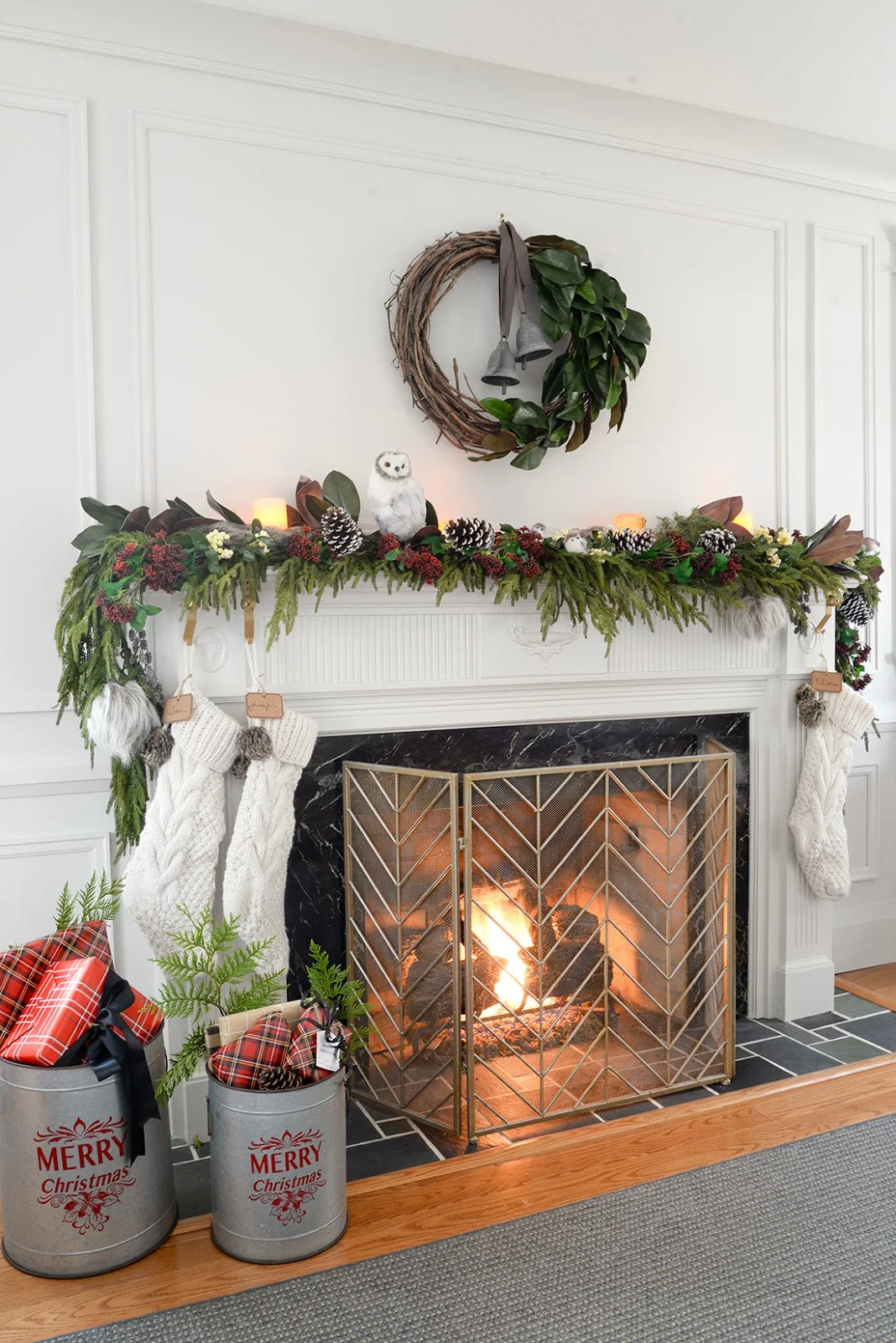 a faux christmas fireplace mantel garland with red seeded eucalyptus, a cedar garland and magnolia leaves. A galvanized bucket holding christmas gifts