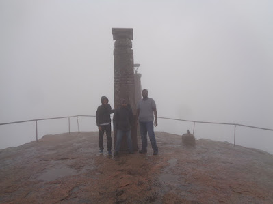 Hikers at the summit of shivagange hanging onto pillars on a windy and foggy day