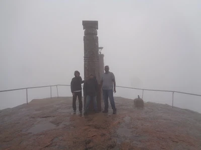 Hikers at the summit of shivagange hanging onto pillars on a windy and foggy day