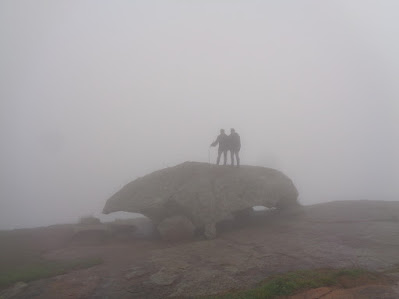 Hikers stand atop a boulder on a very windy and foggy day at shivagange