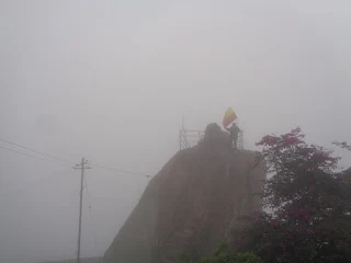 Hiker stands next to Nandi, amidst thick fog on the summit of Shivagange