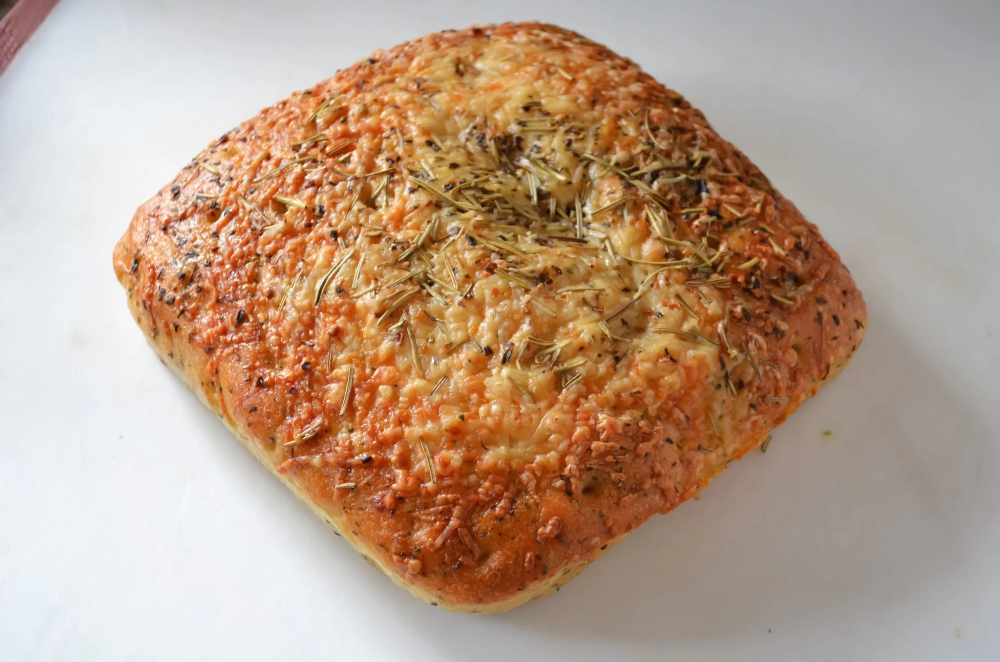A loaf of focaccia bread on a white cutting board.